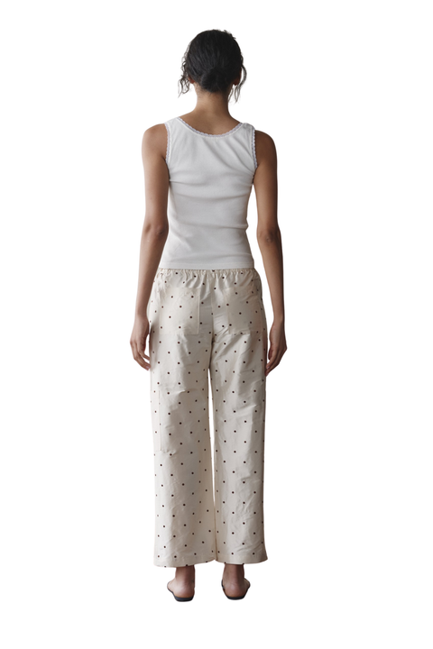 A model shown from the back wearing a white sleeveless top and cream-colored wide-leg pants with a small black polka dot pattern, set against a plain white background.