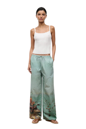 Woman wearing a white sleeveless top and green beach pants on a white background