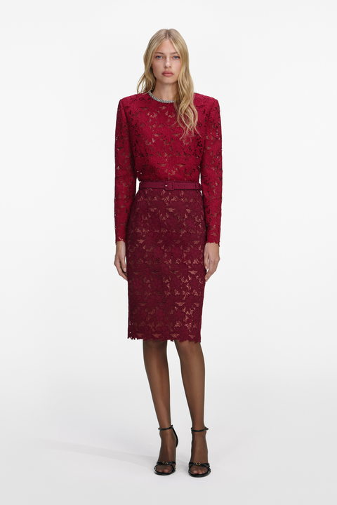 Woman wearing a red lace top with embellishment on the and matching midi skirt on a white background