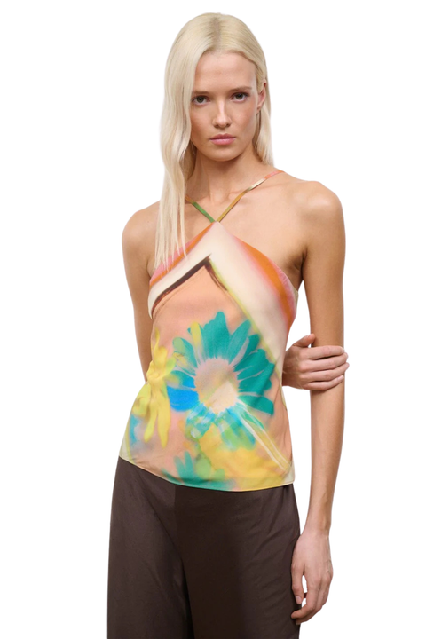 Woman wearing a colorful orange, yellow, and blue sleeveless halter neck top with brown linen pants close up