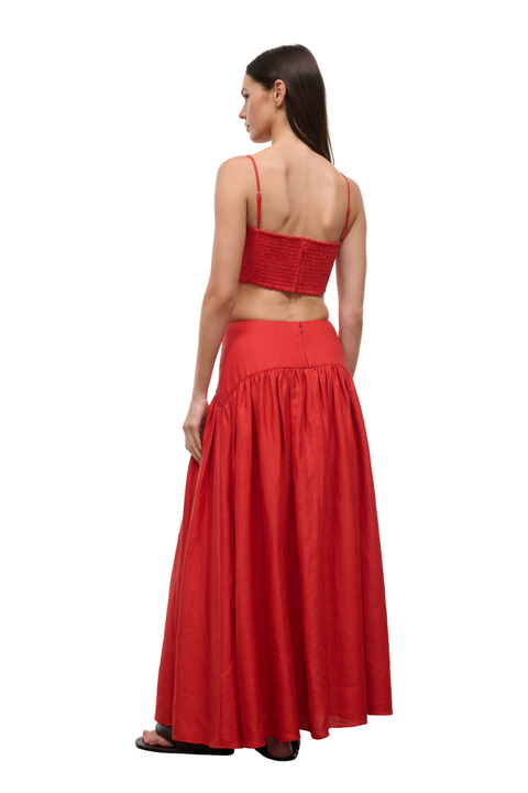 A woman shown from the back wearing a red two-piece outfit consisting of a cropped spaghetti-strap top and a high-waisted, flared maxi skirt, set against a plain white background.