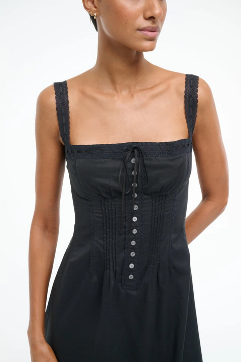 Close up of a woman wearing a black Victorian-inspired midi dress that features lace straps, corset-style detailing, and buttons down the front. 