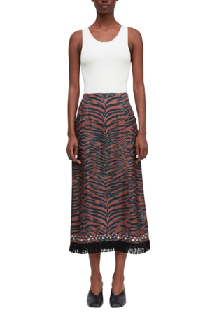 A model wearing a sleeveless white ribbed tank top and a high-waisted midi skirt with a rust-orange and black tiger-stripe pattern and a black lace hem, paired with black pointed flats.