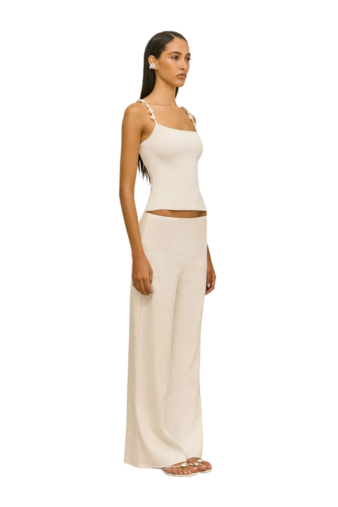 Woman wearing a beige sleeveless top with pearl embellished straps side angle