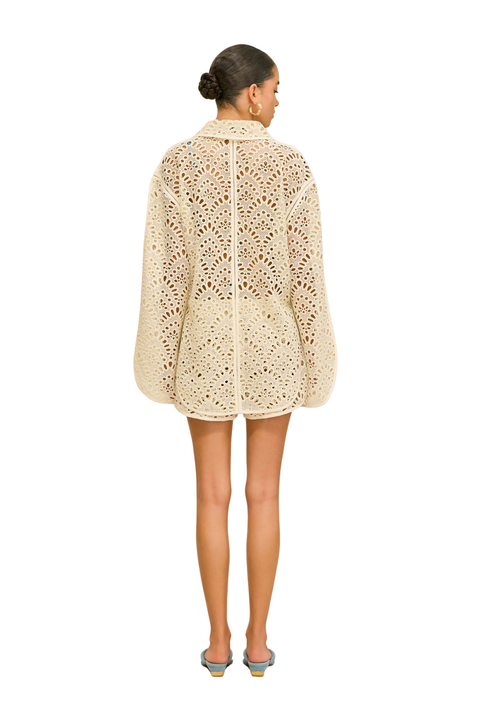 Woman wearing a beige crochet shorts cover-up under a swimsuit back angle