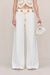 Up close shot of a woman wearing white, white leg jeans that feature a gold chain belt detail, paired with a white crochet top. 