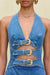 Detail shot of a blue denim mini dress that has a plunging halter neck and three torso cutouts that are adorned with three gold buckles. 