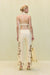 Back angle of a woman wearing a pair of light yellow, mid rise pants that feature a wide leg silhouette with open floral embroidery details on the front and side of the legs, paired with a light yellow top and tote. 