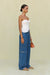 Side view of a woman wearing blue denim high-rise, wide leg jeans that feature cargo pockets and contrast stitching, paired with a white strapless top. 