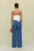 Back view of a woman wearing blue denim high-rise, wide leg jeans that feature cargo pockets and contrast stitching, paired with a white strapless top. 