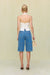 Back view of a woman wearing blue denim cargo shorts in a Bermuda style that hit below the knee, paired with a white off the shoulder top. 