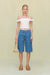Woman wearing blue denim cargo shorts in a Bermuda style that hit below the knee, paired with a white off the shoulder top. 