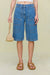 Close up of a woman wearing blue denim cargo shorts in a Bermuda style that hit below the knee, paired with a white off the shoulder top. 