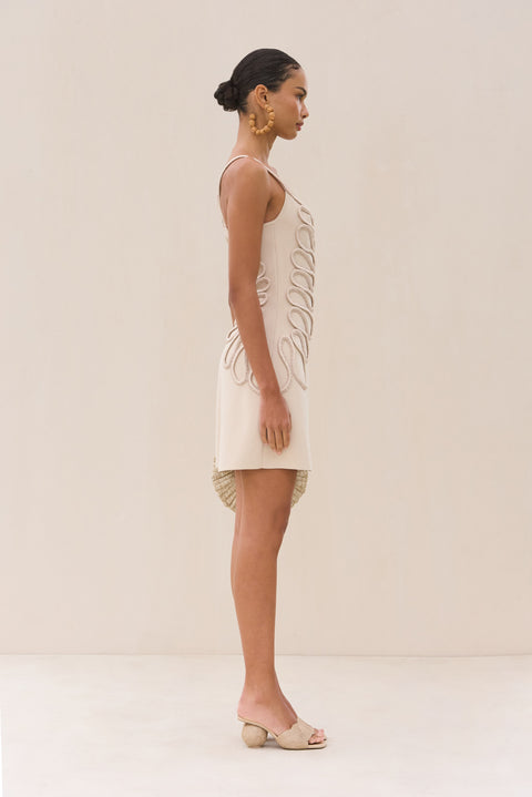 Side view of a woman wearing an ivory knitted mini featuring a swirling rope detail. 