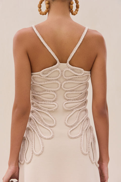 Up close back view of a woman wearing an ivory knitted mini featuring a swirling rope detail. 