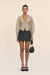 Woman wearing a structured beige cardigan and black skirt holding a black handbag on a beige background