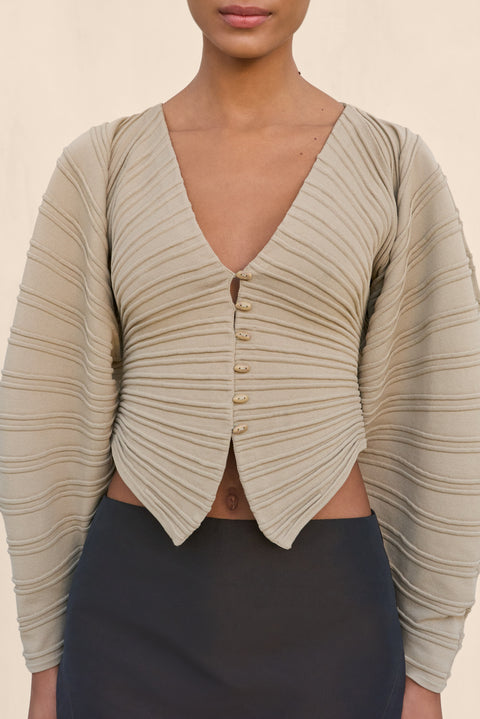 Woman wearing a structured beige cardigan and black skirt holding a black handbag on a beige background