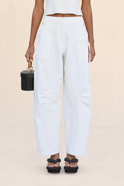 Close up of a woman wearing a pair of white, barrel-leg cargo pants, paired with a white top, black sandals, and black handbag,