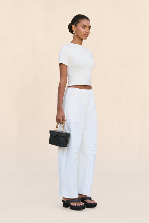 Side-facing woman wearing a pair of white, barrel-leg cargo pants, paired with a white top, black sandals, and black handbag.