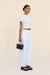 Side-facing woman wearing a pair of white, barrel-leg cargo pants, paired with a white top, black sandals, and black handbag.