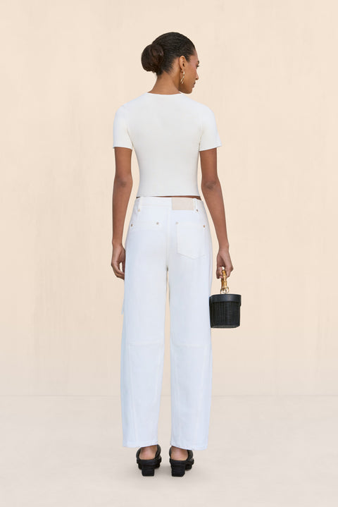 Back-facing woman wearing a pair of white, barrel-leg cargo pants, paired with a white top, black sandals, and black handbag.