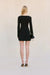 Back-facing woman wearing a black long sleeve mini dress with black heels and a black handbag. 