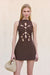 Close up of a woman wearing a brown sleeveless mini dress that features floral cutouts across the body, paired with a tan handbag. 