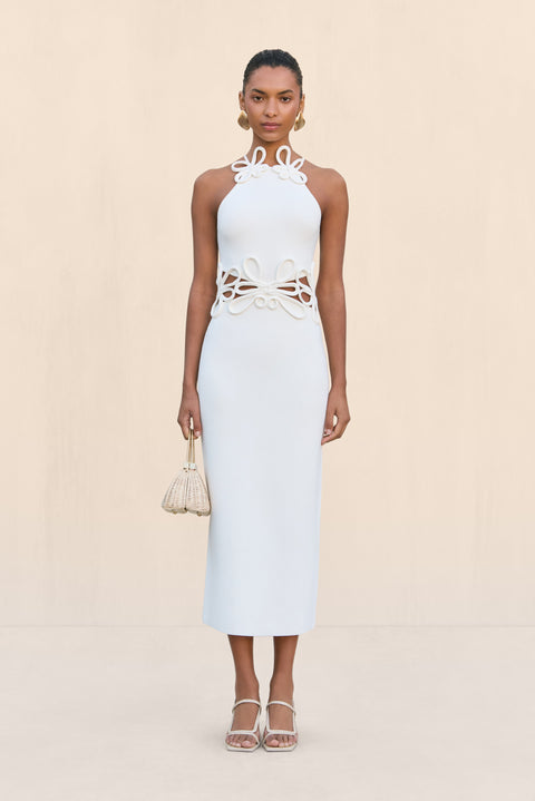 Woman wearing a white knit midi dress that features cutouts at the waist with a floral overlay and a floral applique at the neckline. 