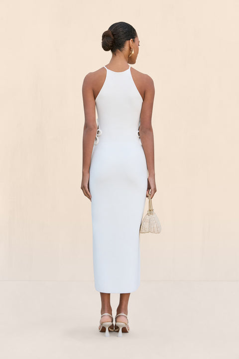 Back-facing woman wearing a white knit midi dress that features cutouts at the waist with a floral overlay and a floral applique at the neckline. 