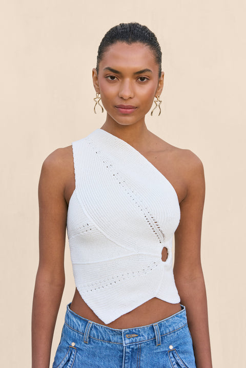 Close up of a woman wearing a white knit one shoulder crop top that features a cutout at the ribcage and an asymmetrical hem. 