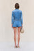 Back view of a woman wearing blue denim cargo shorts paired with a matching denim jacket and a woven handbag. 