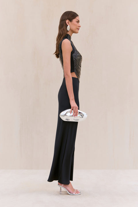 Side-facing woman wearing a black silk maxi skirt paired with a tank top that features black and silver ombre beaded strings draping across the bodice. 