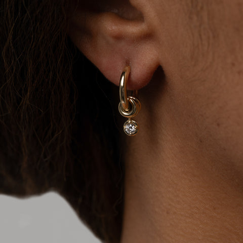 Close up of a woman wearing a Zhara white diamond drop earring. 