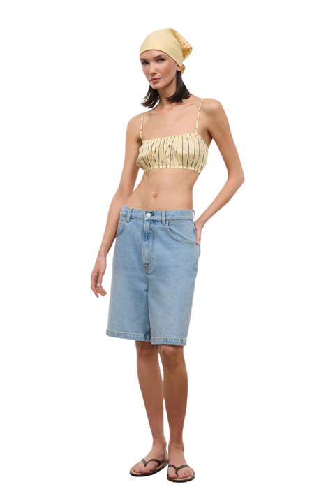 Woman wearing a striped yellow top and denim shorts on a white background