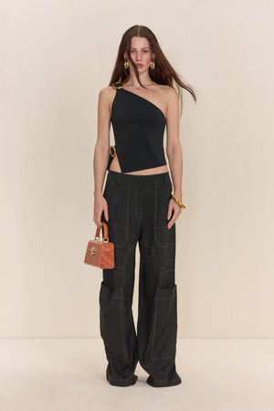 Woman wearing a black asymmetrical top that features gold buckle details on the shoulder and hip, paired with black cargo pants. 