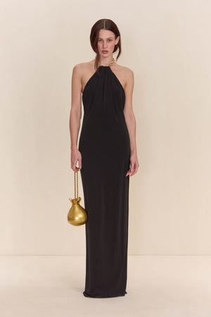 Woman wearing a black gown that features a gold chain halter neck detail. 