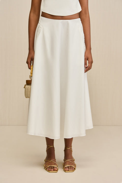 Close up of a woman wearing a white poplin, A-line midi skirt paired with a white top and gold sandals. 