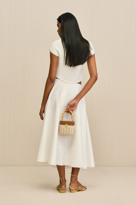Back-facing woman wearing a white poplin, A-line midi skirt paired with a white top and gold sandals. 