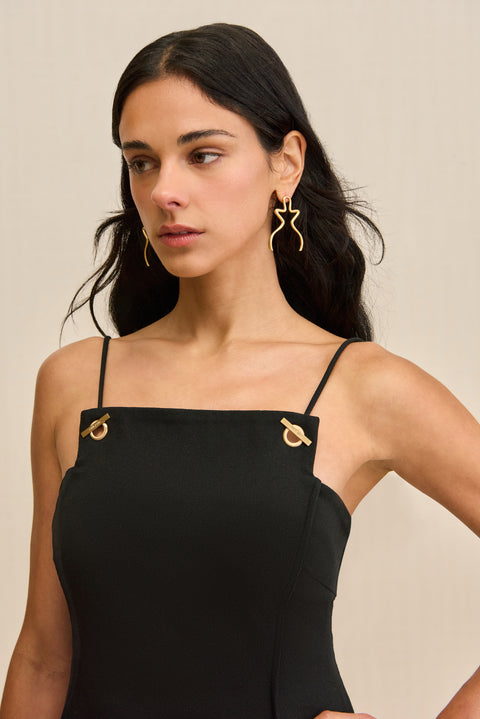 Close up of a woman wearing a black mini dress that features a square neck and grommet-style hardware on the spaghetti straps. 