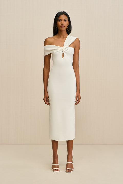 Woman wearing a white knit midi dress that features a twist and keyhole detail at the bust with one strap worn off the shoulder and the other strap worn over the shoulder, paired with white sandals. 