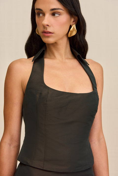 Close up of a woman wearing a dark brown cropped tank top that features a collared halter neck and square neckline, paired with a matching mini skort. 