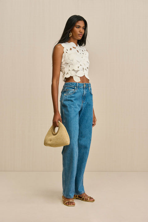 Side-facing woman wearing a white crochet tank top that is crafted from floral appliques sewn together, paired with blue jeans. 