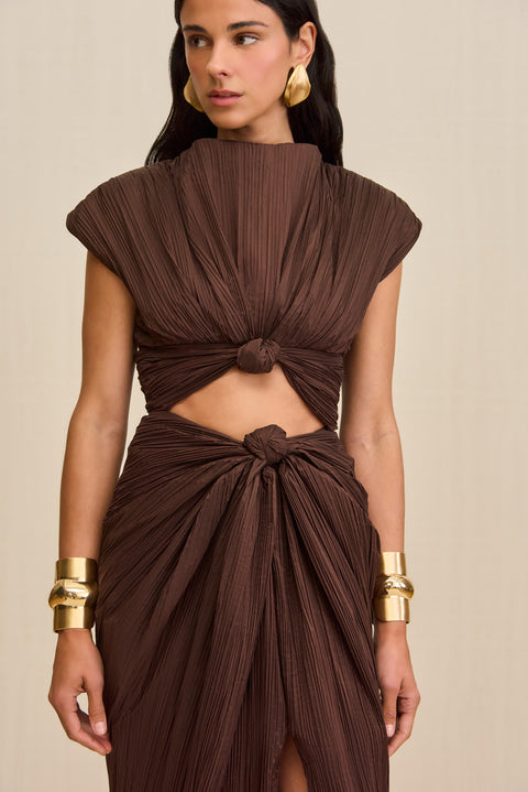 Close up of a Woman wearing a brown structured midi dress crafted from plisse fabric that features a mock neck, front slit, and a knotted cutout detail below the bust. 
