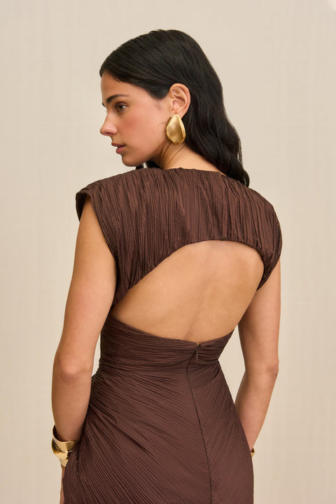 Close up of a back-facing woman wearing a structured brown midi dress crafted from a plisse fabric that features a mock neck and open back design. 