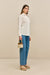 Side-facing woman wearing a white collared button down, paired with blue jeans, tan sandals, and a woven handbag. 