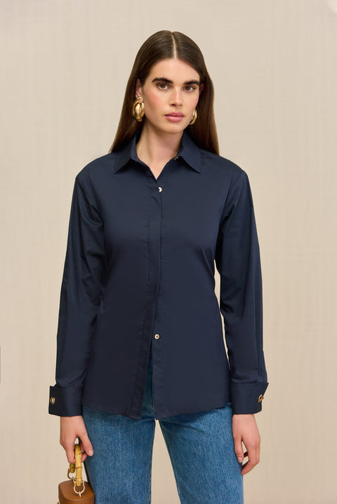 Close up of a woman wearing a navy button-down collared shirt, paired with blue jeans and tan handbag. 
