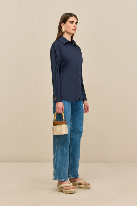Side-facing woman wearing a navy button-down collared shirt, paired with blue jeans and tan sandals. 
