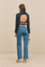 Back-facing woman wearing a navy collared shirt that features an open back secured by two adjustable buckle straps , paired with blue jeans and tan sandals. 