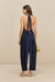 Back-facing woman wearing navy blue, utility-style barrel leg pants, with minimal gold-toned hardware, paired with a navy top and tan sandals. 