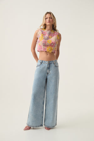 Woman wears floral embellished crop top with low rise jeans.